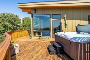 A wooden deck with a hot tub, potted plants, and a view of the surrounding area. - Full Downtown Anchorage Triplex for Large Groups (Anchorage)
