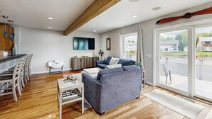 A modern living room with a sofa, dining area, and a large window with a view. - Elegant Anchorage Lakehouse w/ Direct Water Access (Anchorage)
