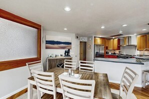 Ein Essbereich mit einem Holztisch und weißen Stühlen, eine Küche mit Holzschränken und Edelstahlgeräten sowie ein Bild an der Wand.