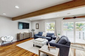 Ein modernes Wohnzimmer mit Holzboden, einem blauen Sofa, einem weißen Sessel, einem Couchtisch und einem an der Wand befestigten Fernseher.