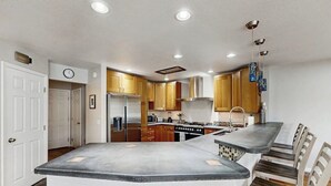 A kitchen with a central island, wooden cabinets, stainless steel appliances, and a dining area with chairs. - Elegant Anchorage Lakehouse w/ Direct Water Access (Anchorage)