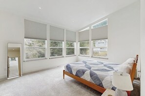 A bedroom with a bed, a bedside lamp, and a window with blinds.