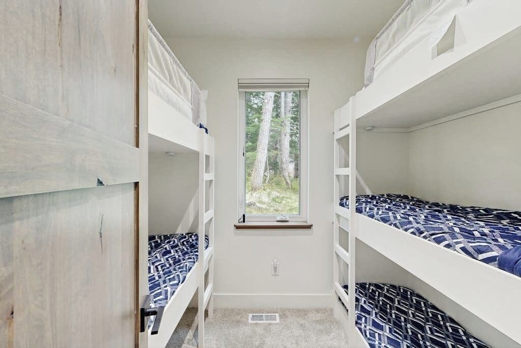 A narrow room with bunk beds, a window, and a door.