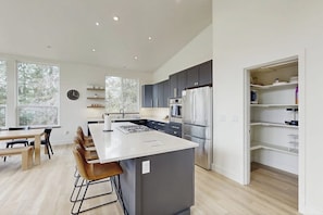A modern kitchen with a central island, stainless steel appliances, and a view of the outdoors through large windows.