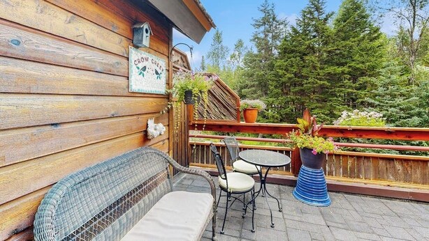A wooden exterior wall with a sign, a wicker sofa, two chairs, a small round table, and potted plants. - Glacier-view Studio w/ Its Own Private Entrance (Girdwood)