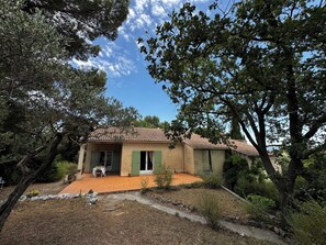 A rustic house with a tiled roof, a patio with a table and chairs, surrounded by trees and shrubs. - Family villa with a pool and garden, featuring a view (Caumont-sur-Durance)
