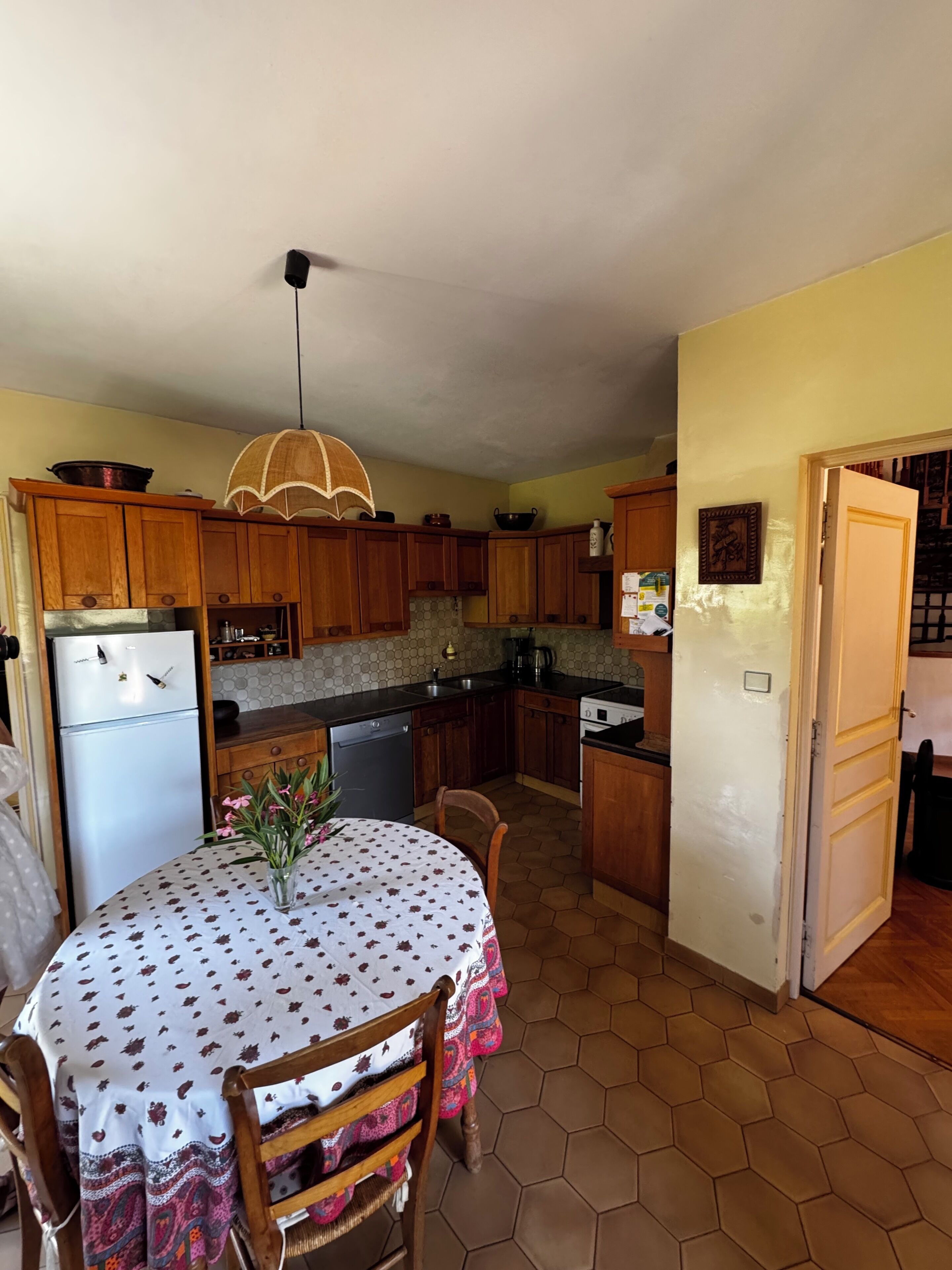 Eine Küche mit Holzausstattung, einem weißen Kühlschrank, einem Esstisch mit Blumenmuster und einer Pendelleuchte.