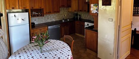 Eine Küche mit Holzausstattung, einem weißen Kühlschrank, einem Esstisch mit Blumenmuster und einer Pendelleuchte.