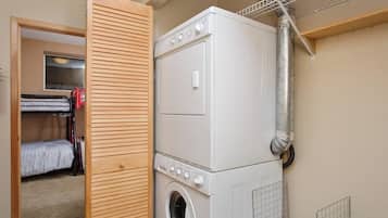A laundry room with stacked washing machines and dryers, a wooden door, and a metal vent.