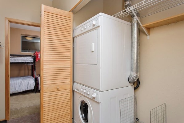 A laundry room with stacked washing machines and dryers, a wooden door, and a metal vent.