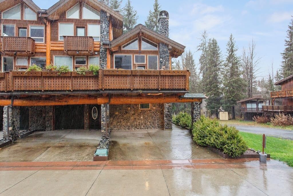 A large wooden house with a stone foundation, a covered deck, and a driveway.