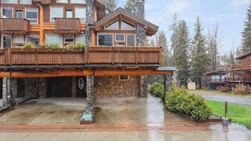 A large wooden house with a stone foundation, a covered deck, and a driveway.