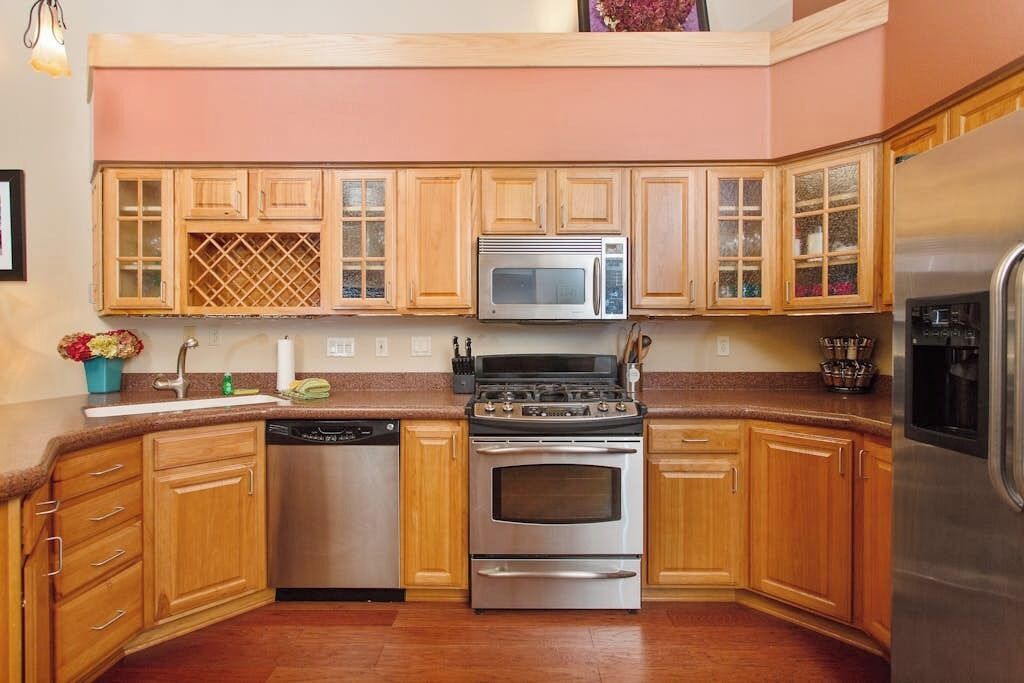Una cocina con armarios de madera, un refrigerador de acero inoxidable, microondas, lavavajillas y estufa.