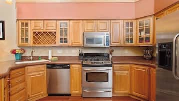 Una cocina con armarios de madera, un refrigerador de acero inoxidable, microondas, lavavajillas y estufa.