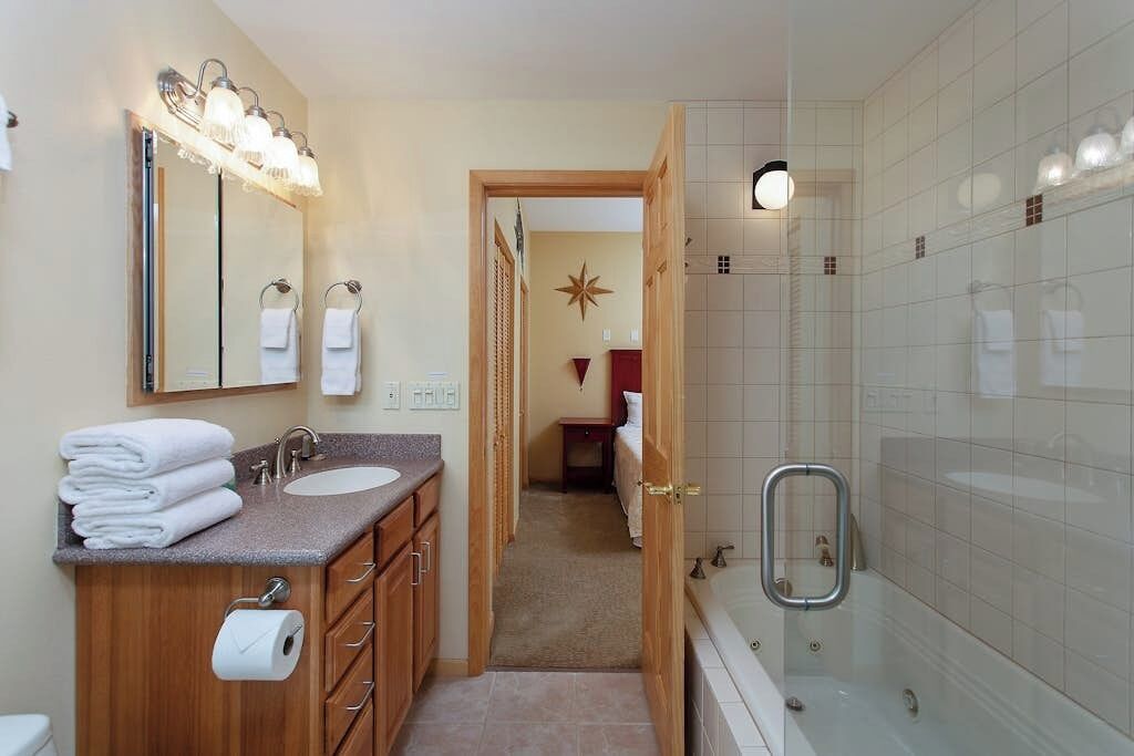 A bathroom with a double sink, a mirror with lights, a shower with a glass door, and a towel rack.