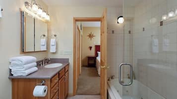 A bathroom with a double sink, a mirror with lights, a shower with a glass door, and a towel rack.