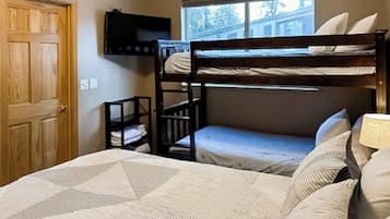 A room with bunk beds, a small desk, a window, and a door.