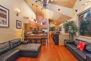 A spacious living area with a large L-shaped black leather sofa, a wooden ceiling, and a kitchen in the background. - Contemporary Girdwood Townhome Across From Alyeska (Girdwood)