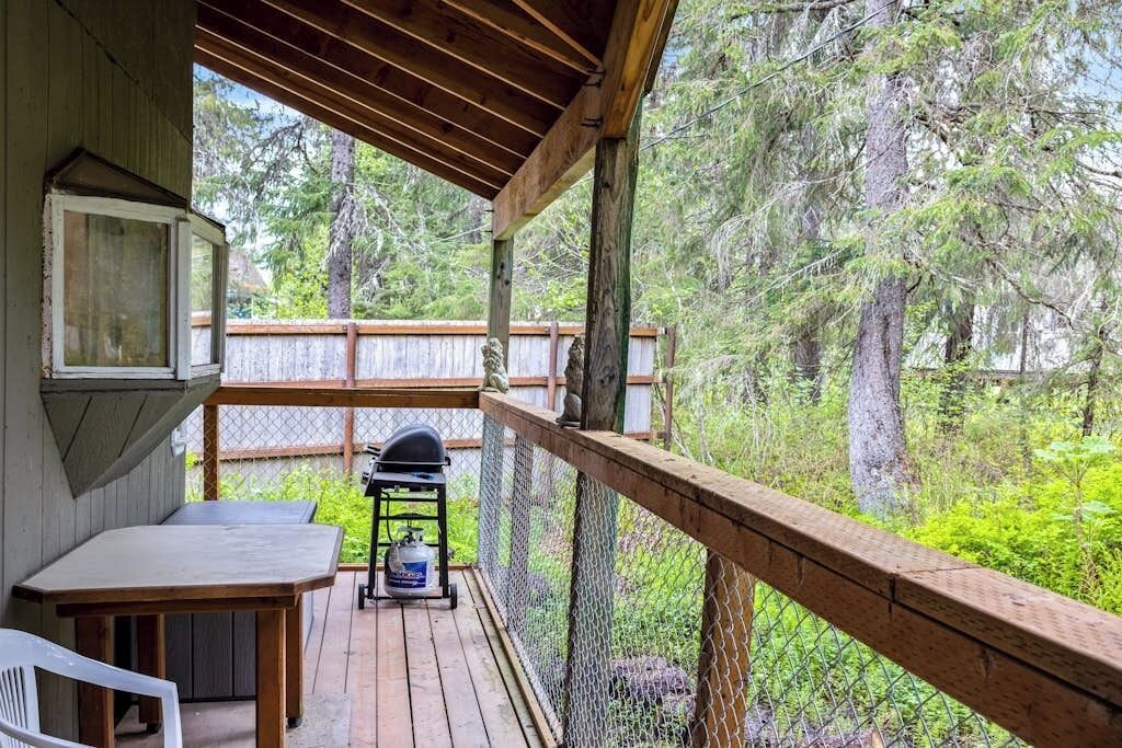 A wooden deck with a table and chairs, a grill, and a view of a forested area.