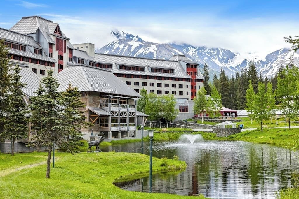 A hotel with a mountain backdrop, a pond, and a statue.