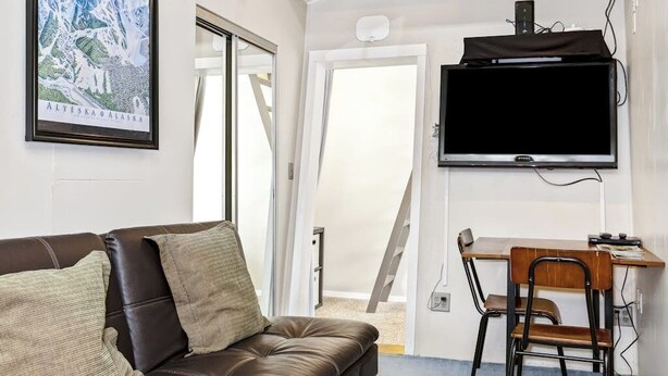 Una habitación con un sofá de cuero marrón, un escritorio de madera con dos sillas, un televisor montado y un mapa enmarcado en la pared.