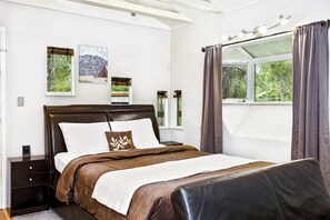 Ein Schlafzimmer mit Bett, Nachttischen, einem Fenster mit Vorhängen und Wandbildern.