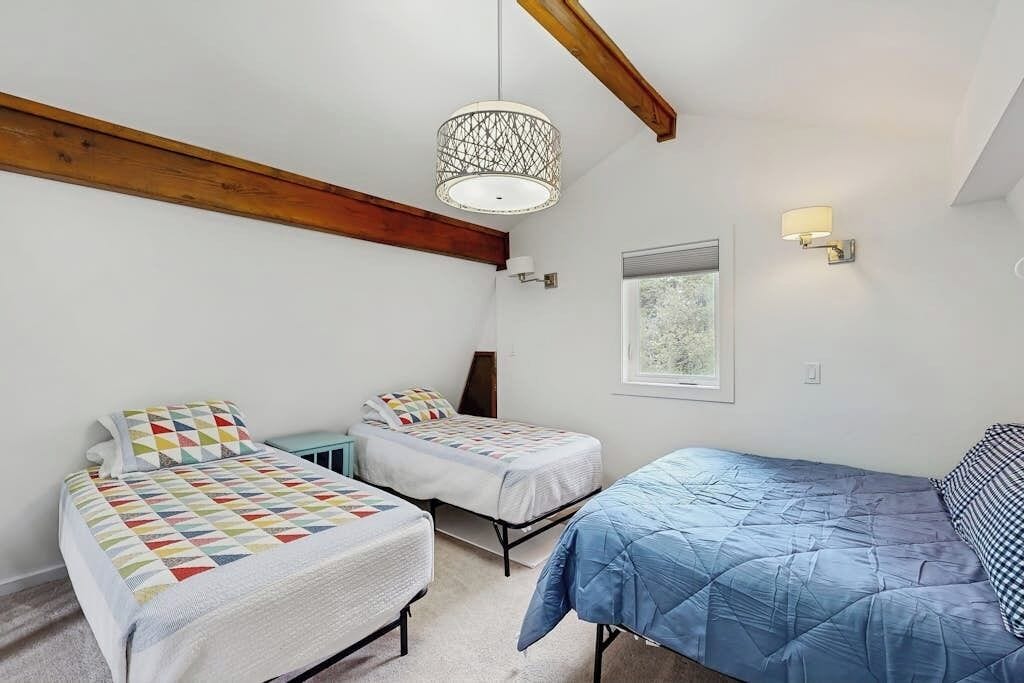 Un dormitorio con dos camas individuales, un ventanal con vistas y una lámpara colgante.