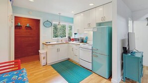 Una cocina compacta con armarios blancos, un refrigerador verde azulado y una ventana que deja entrar luz natural.