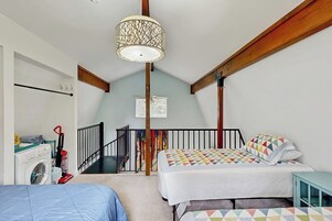 Un dormitorio con cama, lavadora, lámpara en el techo y escalera.