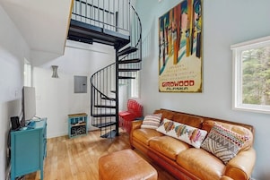 A living room with a brown leather sofa, a teal cabinet, a red chair, and a black spiral staircase.