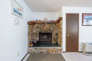 A stone fireplace with a wooden mantel, a door to the right, and a framed picture above it.