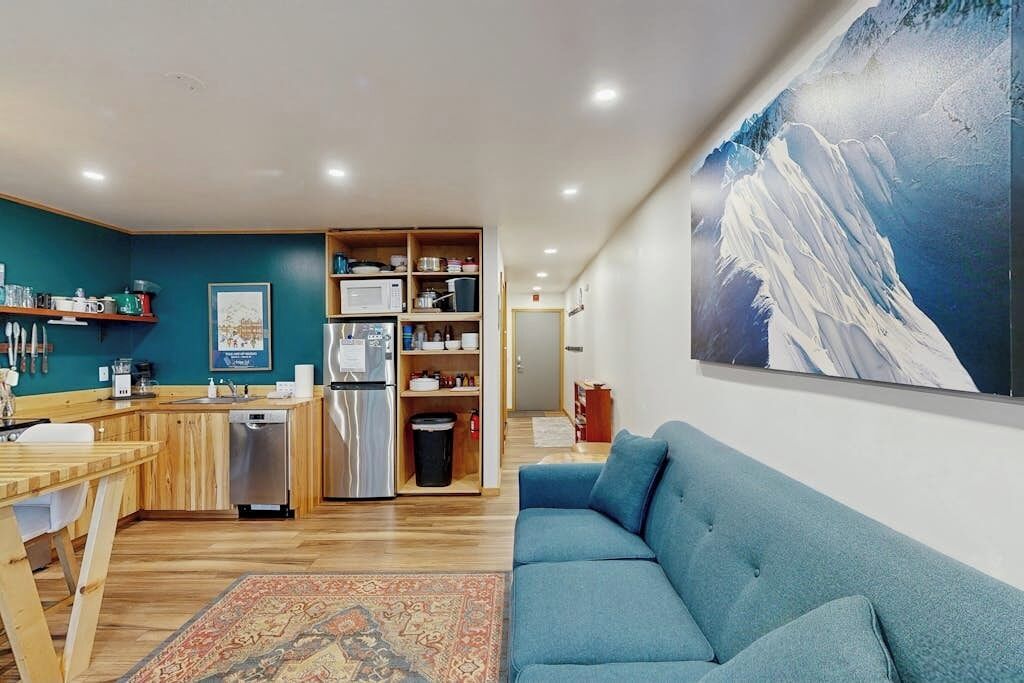 A modern kitchen with a microwave, refrigerator, and wooden cabinets. There is a blue sofa and a rug in the living area.