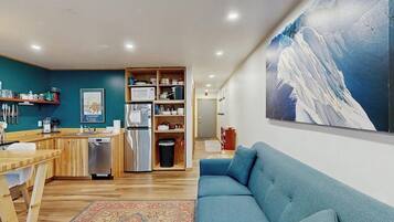 A modern kitchen with a microwave, refrigerator, and wooden cabinets. There is a blue sofa and a rug in the living area.