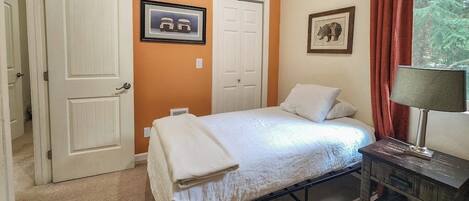 Un dormitorio con una cama, dos puertas, una lámpara y un cuadro en la pared.