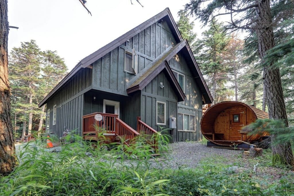 A cabin with a steeply pitched roof, a wooden deck, and a large cylindrical structure.