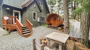 A cabin with a wooden staircase leading to a porch, a log cabin structure, and a table with a bench. - Girdwood Lodge w/ Sauna, Near Alyeska Resort (Girdwood)