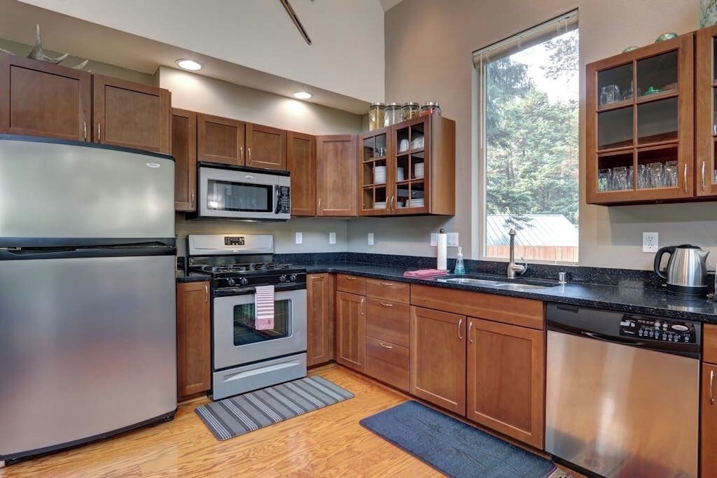 A modern kitchen with stainless steel appliances, wooden cabinets, and a large window providing natural light.