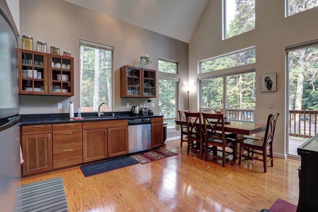 A kitchen with wooden cabinets, a dining area with a table and chairs, and large windows allowing natural light.