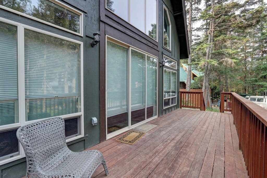 A wooden deck with a chair, large windows, and a view of trees.