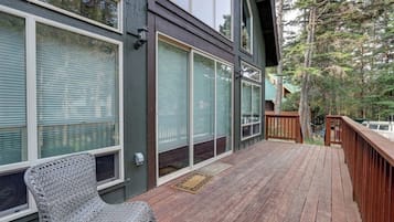 A wooden deck with a chair, large windows, and a view of trees.