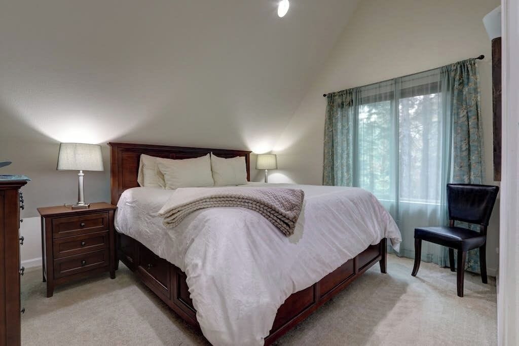 A bedroom with a large bed, two bedside tables with lamps, a chair, and a window with curtains.