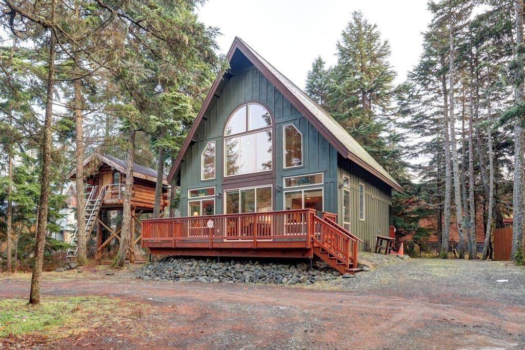 A cabin with a wooden deck, surrounded by trees.