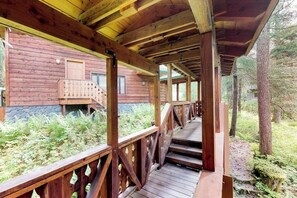 A wooden deck leading to a cabin with a stone foundation, surrounded by greenery.