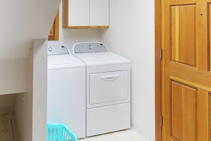 A laundry room with a front-loading washer and dryer, a wooden door, and a white wall.