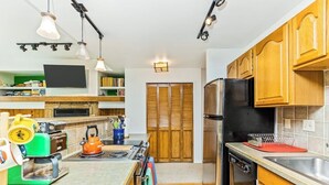 Cocina moderna con estufa, horno y refrigerador. Se observa un armario de madera y un microondas.