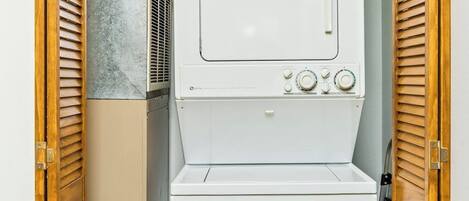 A compact, white laundry room with a built-in washer and dryer, wooden louvered doors, and a tiled wall.