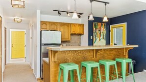 Una cocina con armarios de madera, una barra y taburetes verdes.