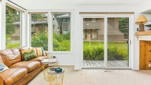 Una sala de estar moderna con un sofá de cuero, una pequeña mesa redonda y vistas a una terraza de madera a través de puertas correderas de vidrio.
