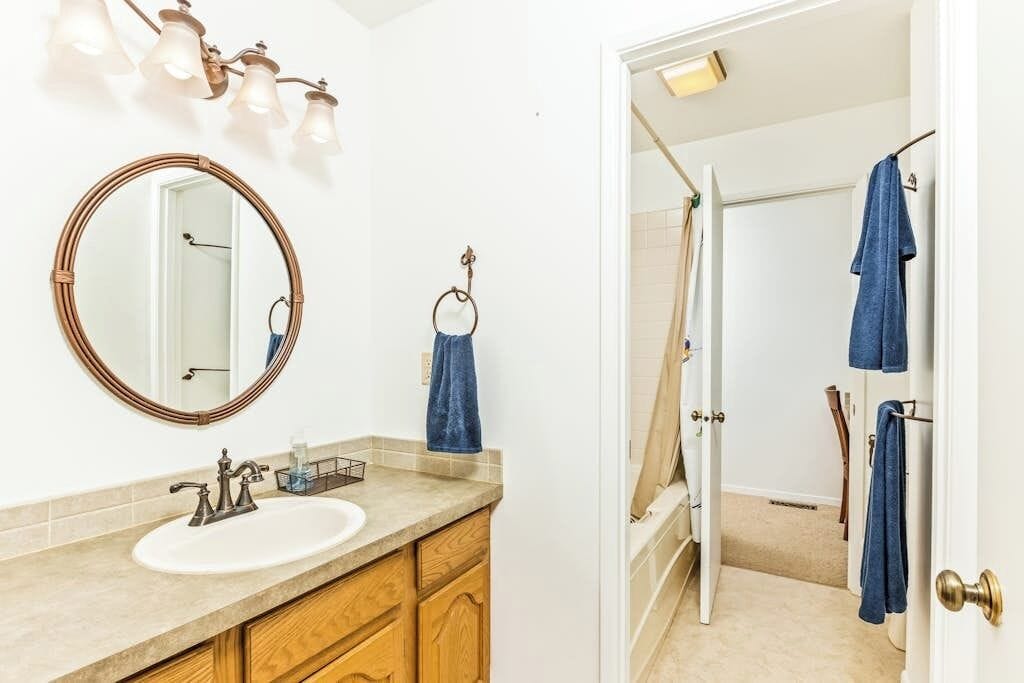A bathroom with a round mirror, a sink, wooden cabinets, and a shower area with towels.