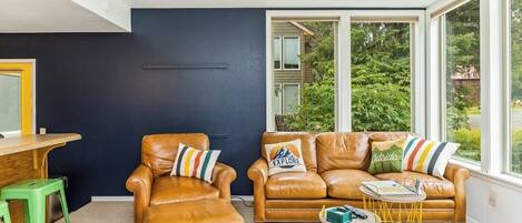 Una sala de estar moderna con sofás de cuero, una mesita redonda y vistas a la vegetación exterior.